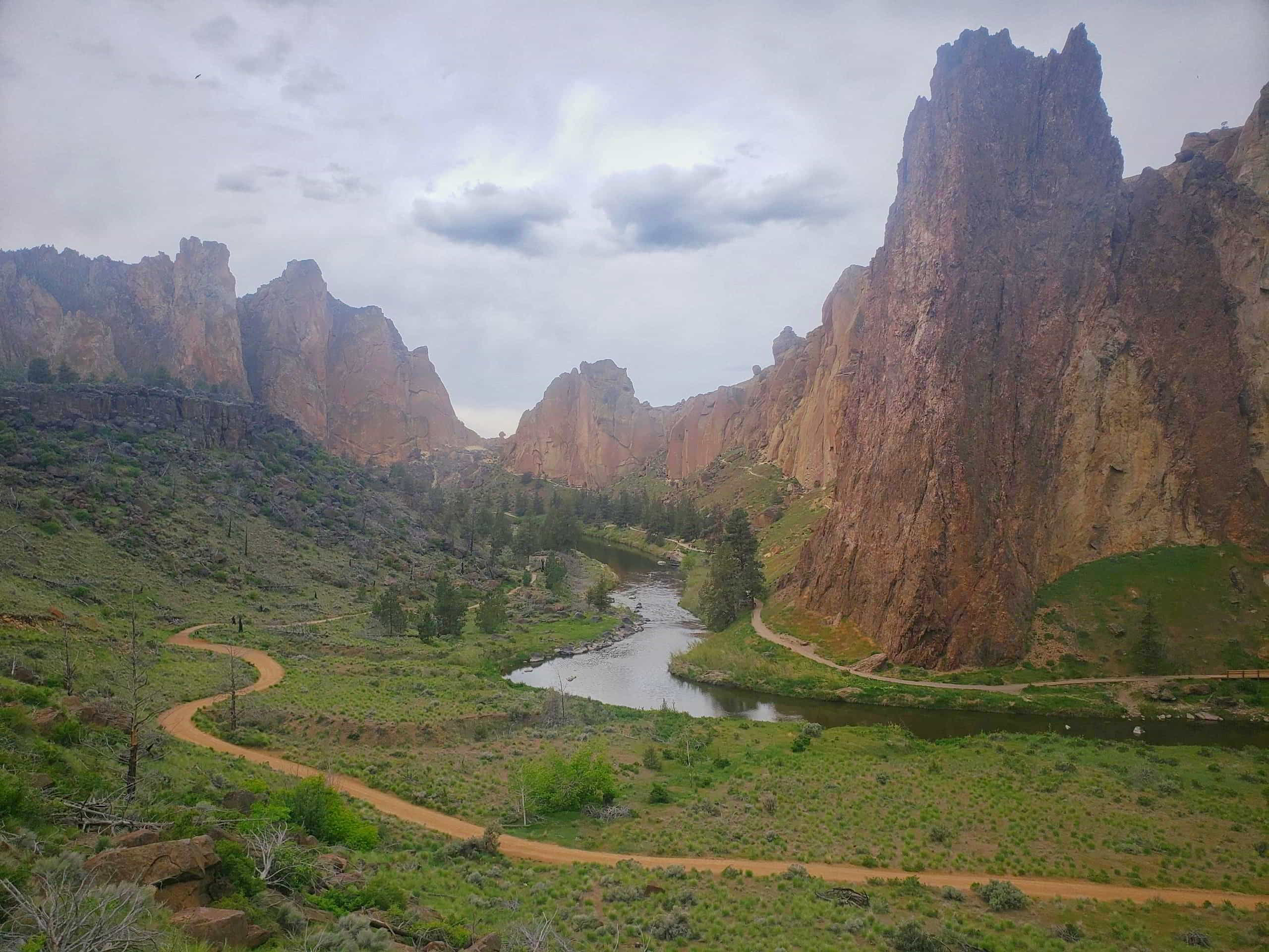 Smith rock, with a red path winding in the foreground, and the river and jagged rocks in the background